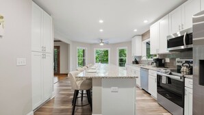 A modern kitchen with white cabinets, stainless steel appliances, and a central island with bar stools. - Porch Paradise by Avantstay New Pool, Firepit (Mooresville)