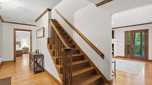 A staircase with wooden steps and a handrail, a bedroom with a bed and nightstand, and a view of the outdoors through a glass door. - Porch Paradise by Avantstay New Pool, Firepit (Mooresville)