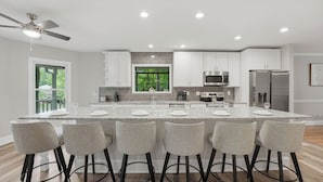 A modern kitchen with a central island, bar stools, and a view of greenery outside. - Porch Paradise by Avantstay New Pool, Firepit (Mooresville)