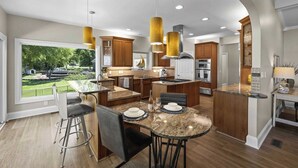 Une cuisine moderne dotée d’un grand îlot central, de luminaires suspendus et offrant une vue sur l’ext érieur.