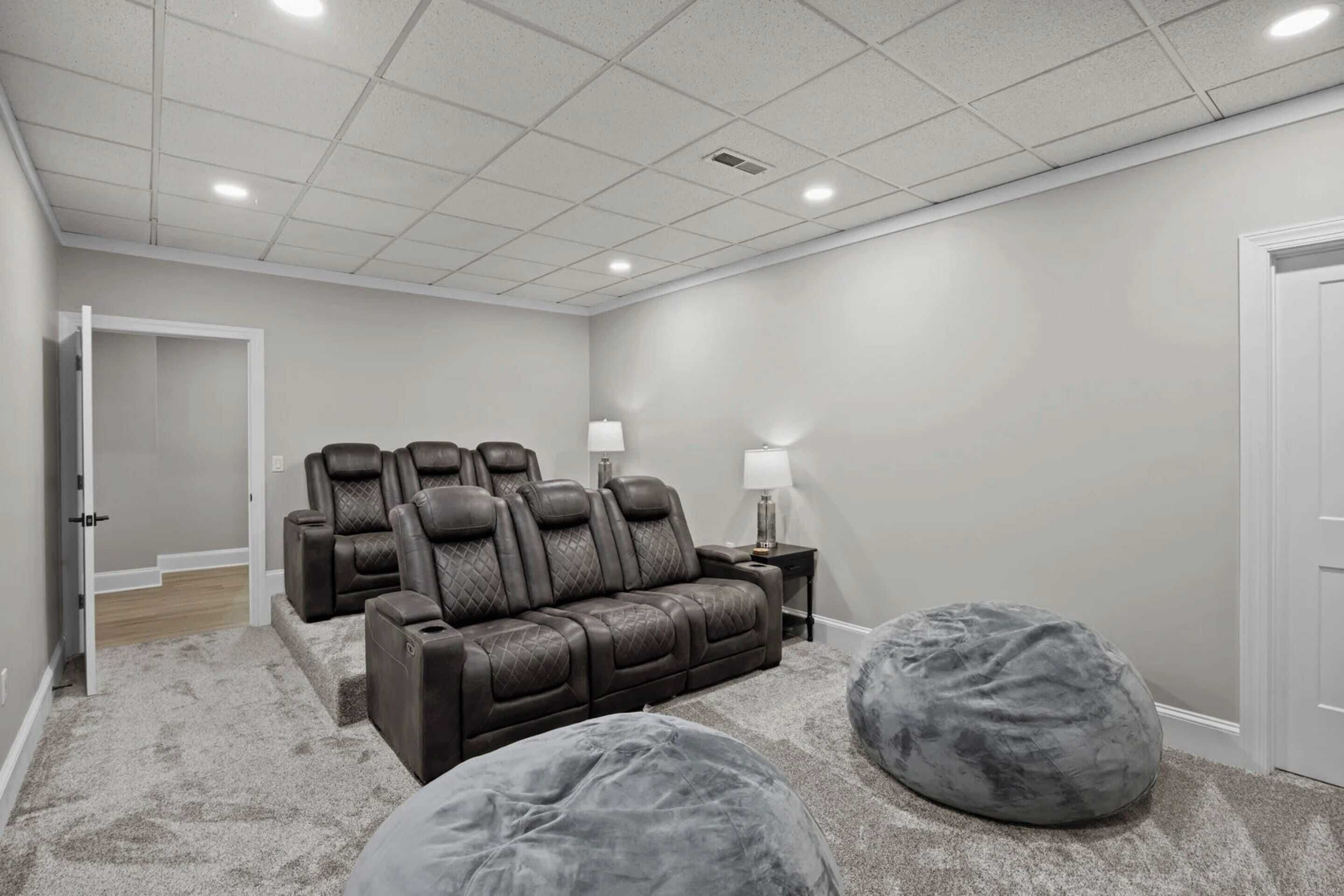 A home theater room with a brown leather sofa, two bean bags, and a white door.