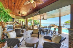 A covered outdoor area with wicker furniture, a stone fireplace, and a view of the ocean. - Water, Water Everywhere by Avantstay Pool + Dock (Mooresville)