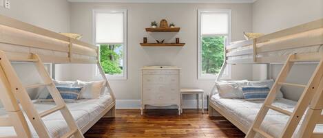Una habitación con dos literas, un aparador y dos ventanas con persianas.
