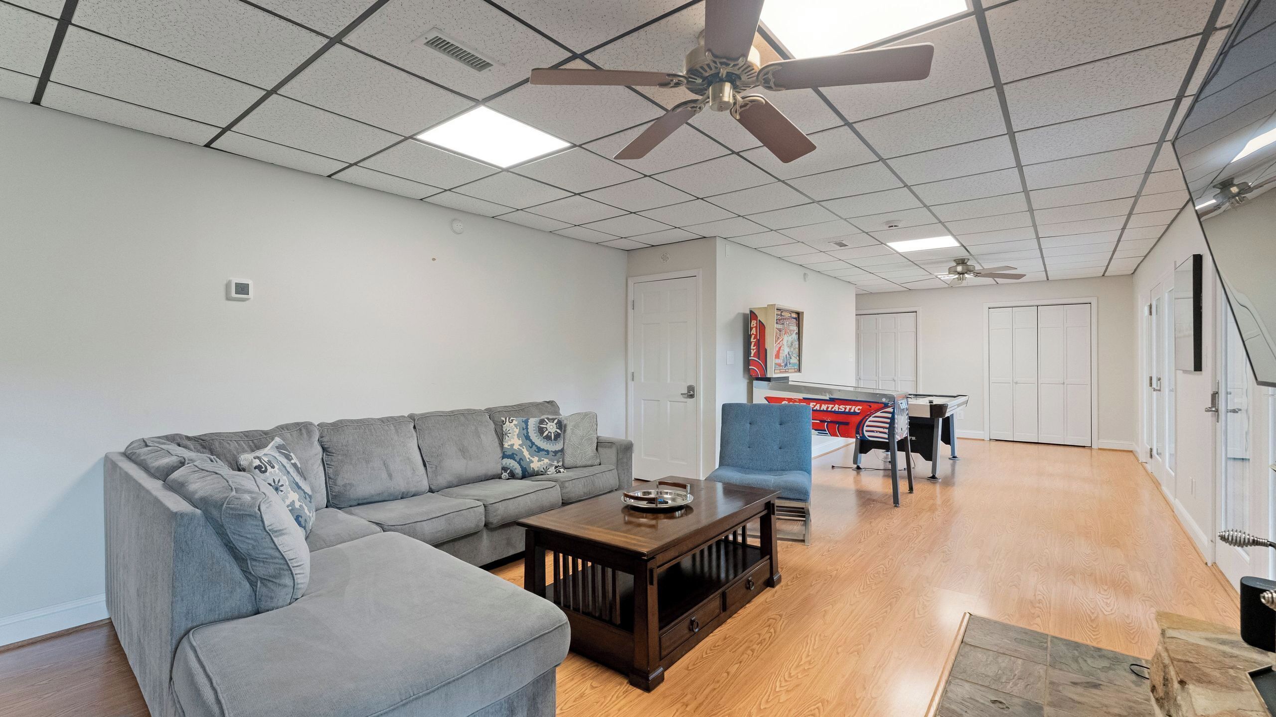 A living room with a grey sofa, a wooden coffee table, a blue chair, and a pool table.