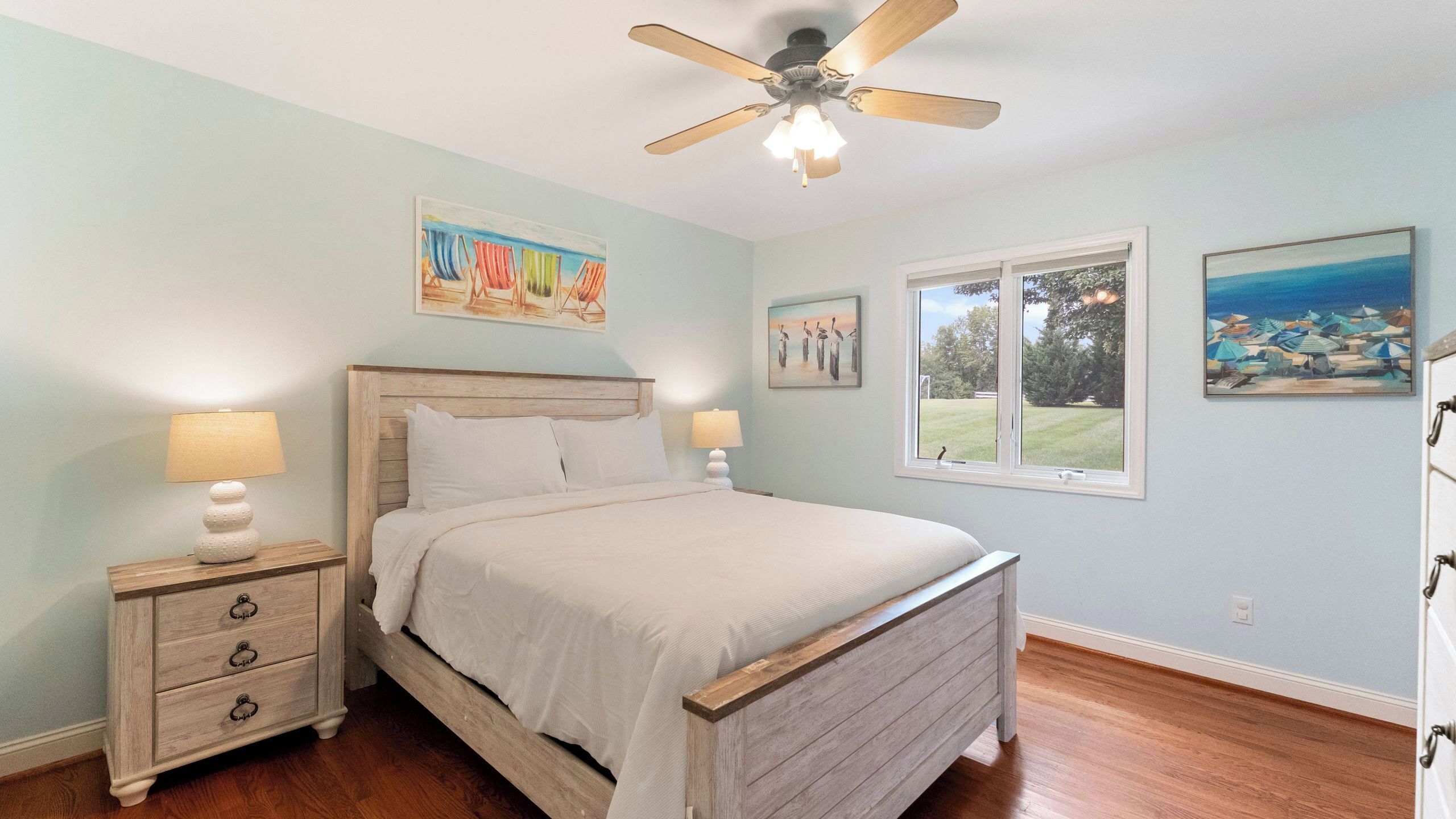 A bedroom with a bed, two bedside tables, a ceiling fan, and two windows.