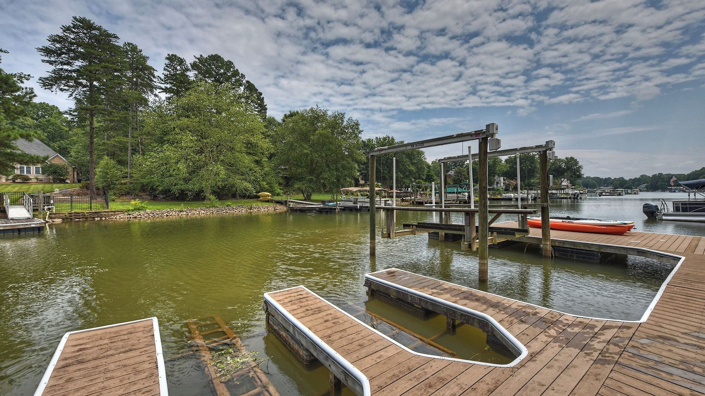 A wooden dock with a boat, a wooden pier, and a calm lake surrounded by trees.