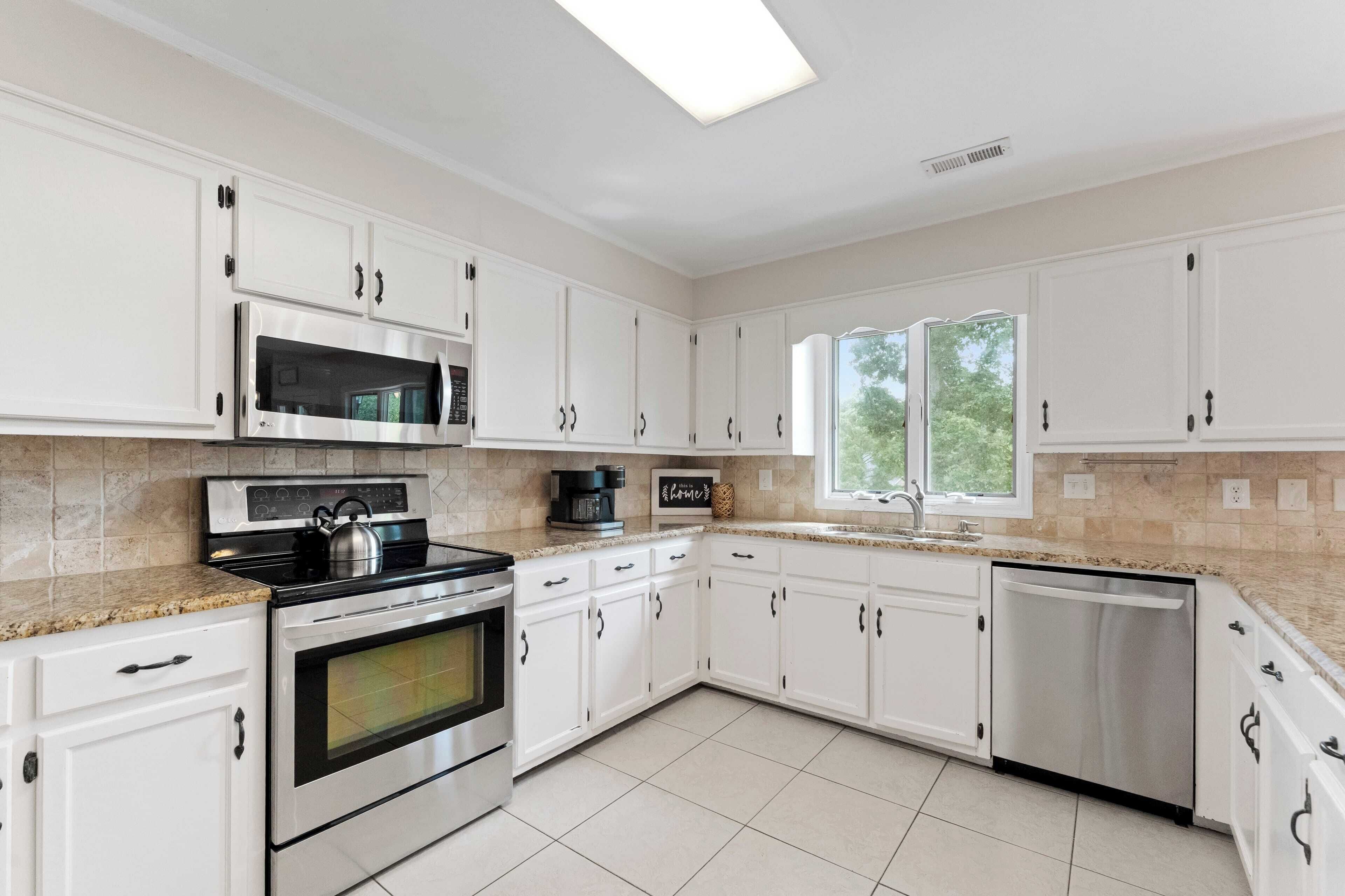 A modern kitchen with white cabinets, stainless steel appliances, and a window providing natural light.