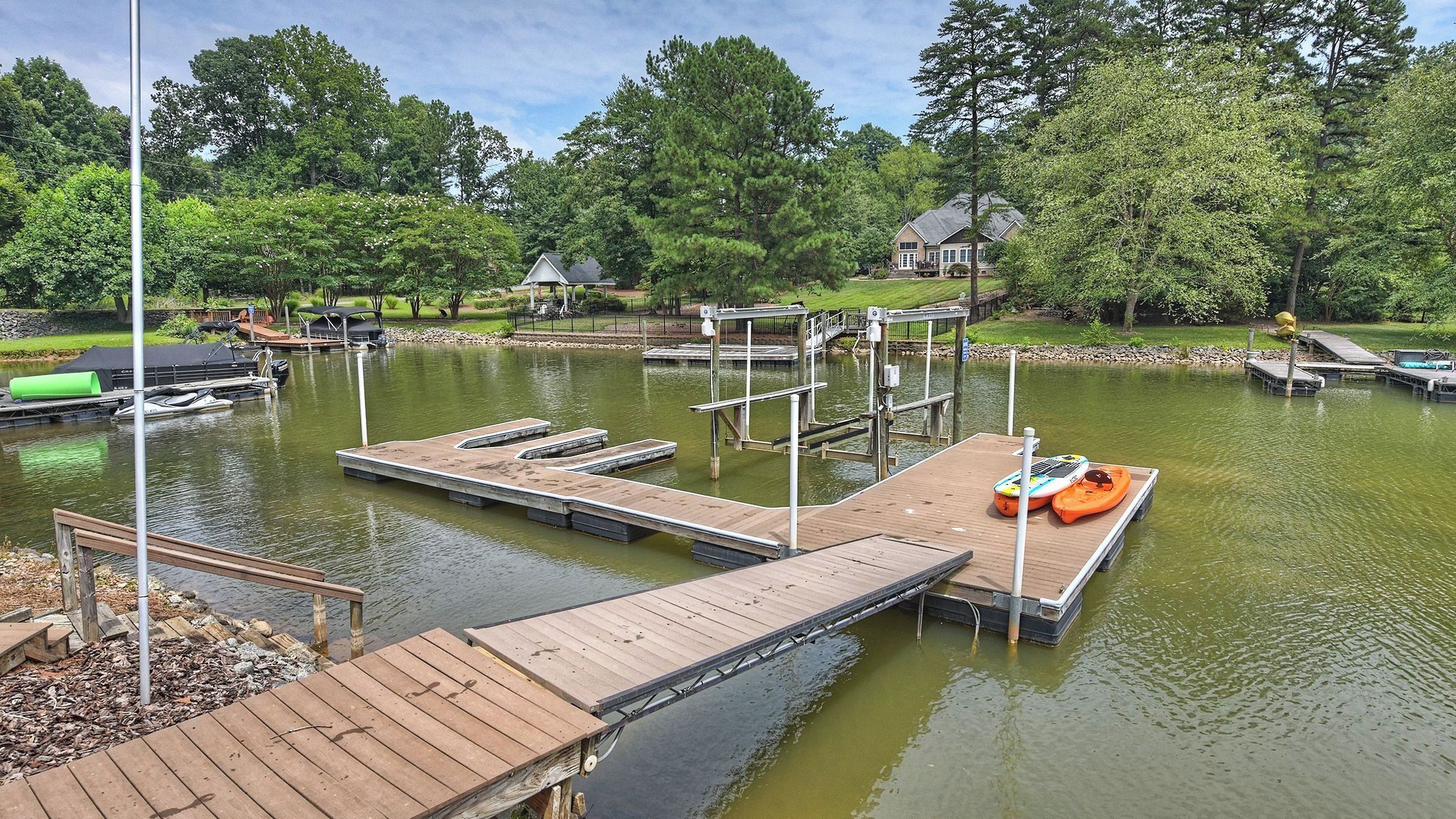 A lakeside dock with kayaks, a boat, and a house in the background.