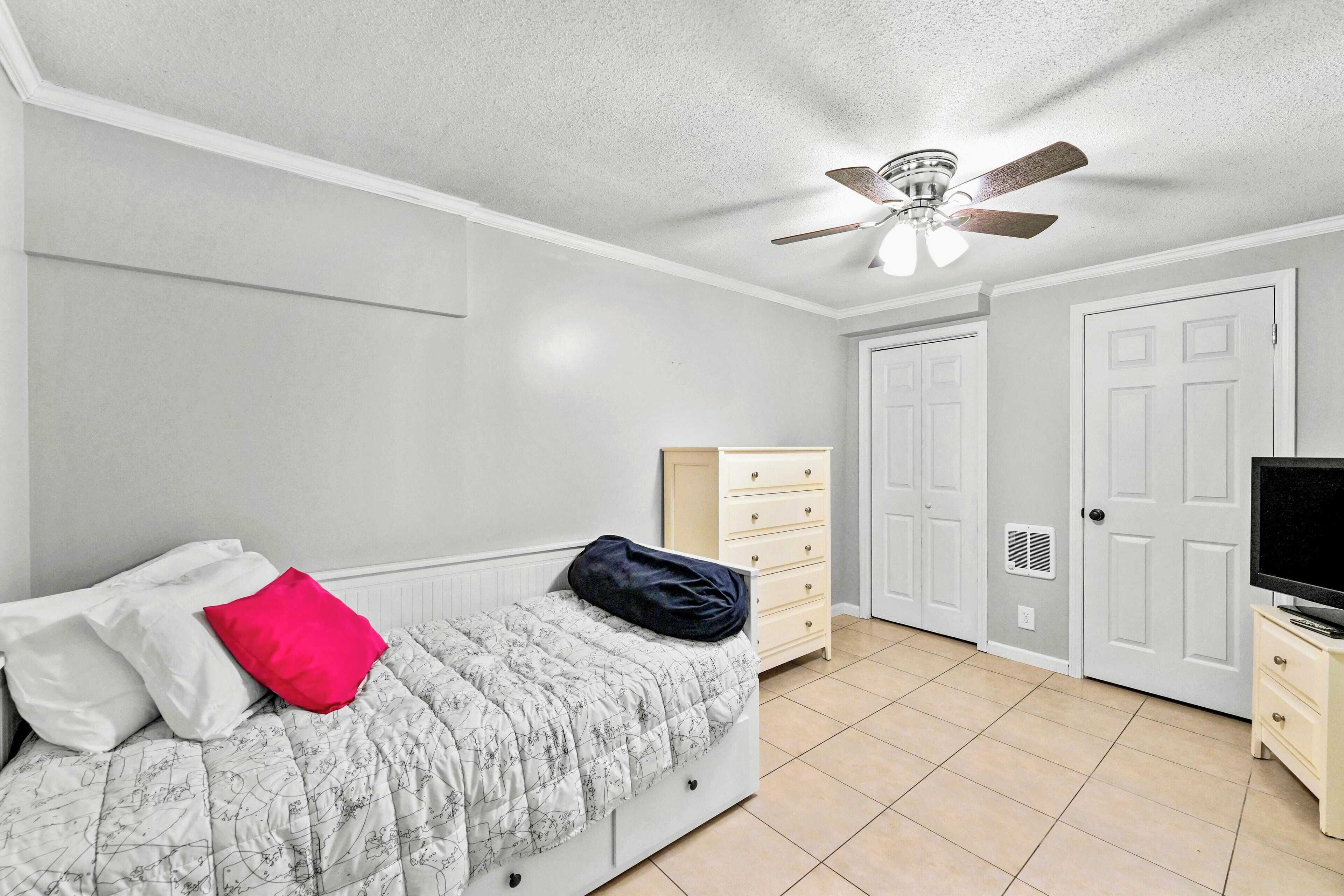 A bedroom with a bed, a ceiling fan, a dresser, a television, and a door.