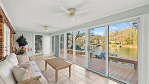 A spacious room with a sliding glass door leading to an outdoor deck, a ceiling fan, and a view of a lake. - Dock Days by Avantstay Swimming Platform, Dock (Denver)