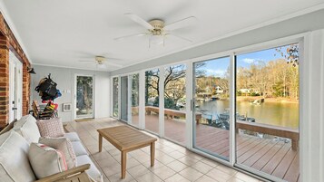 Una habitación amplia con puerta de vidrio corredera que da a una terraza exterior, ventilador de techo y vista a un lago.