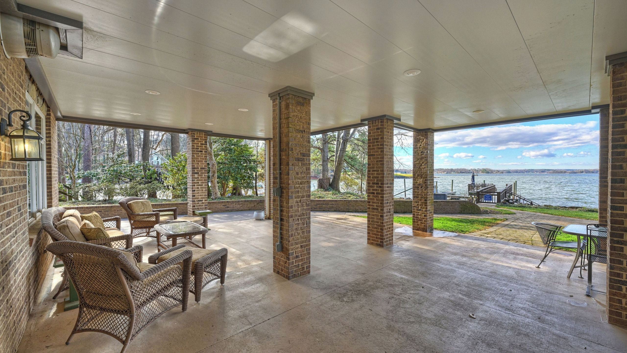 A covered patio with wicker furniture, brick pillars, and a view of a lake.
