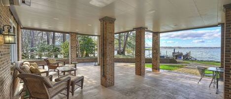 A covered patio with wicker furniture, brick pillars, and a view of a lake.