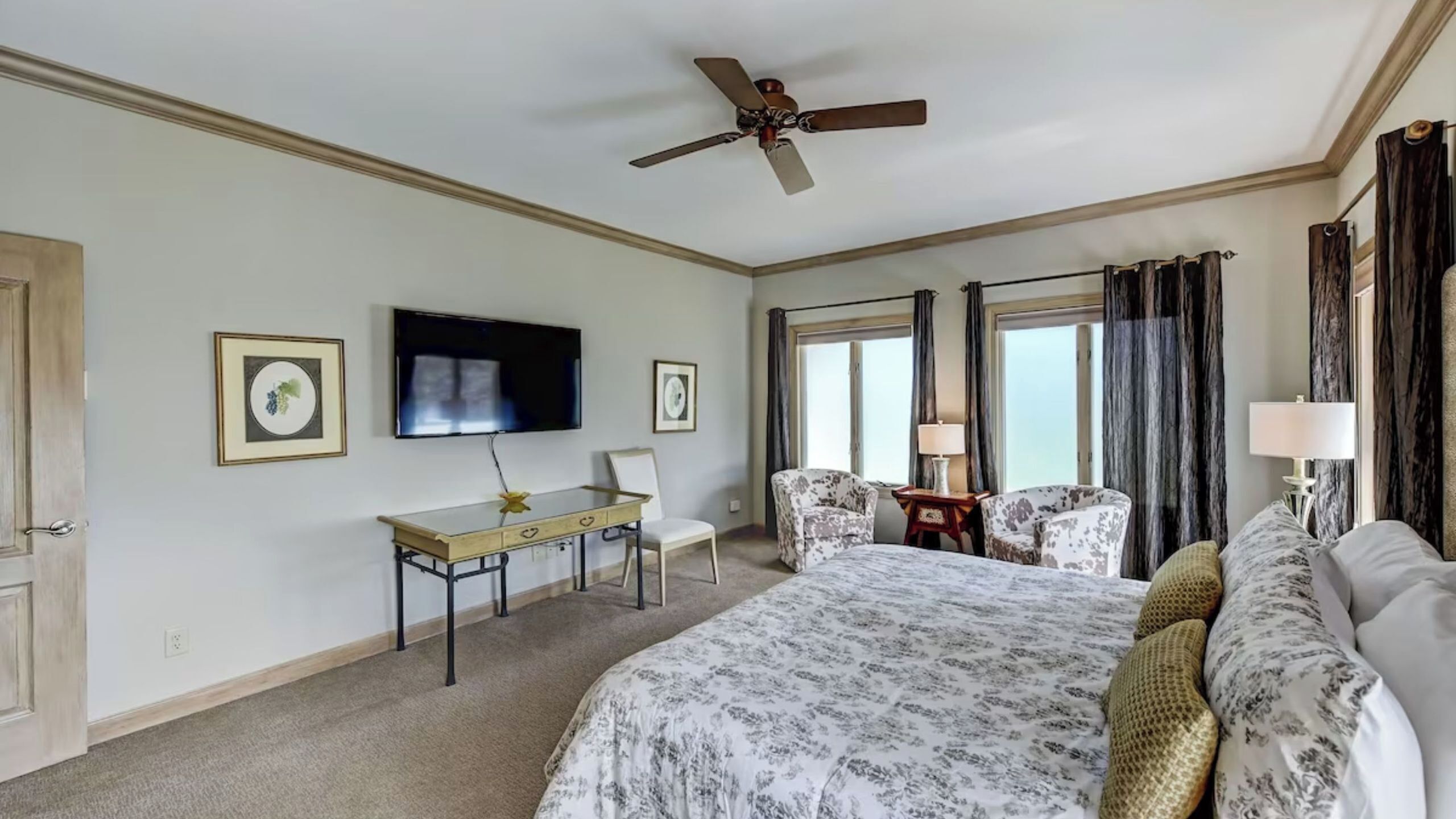 Une chambre d’hôtel équipée d’un lit, d’un bureau, de chaises, d’une télévision et d’un ventilateur de plafond.