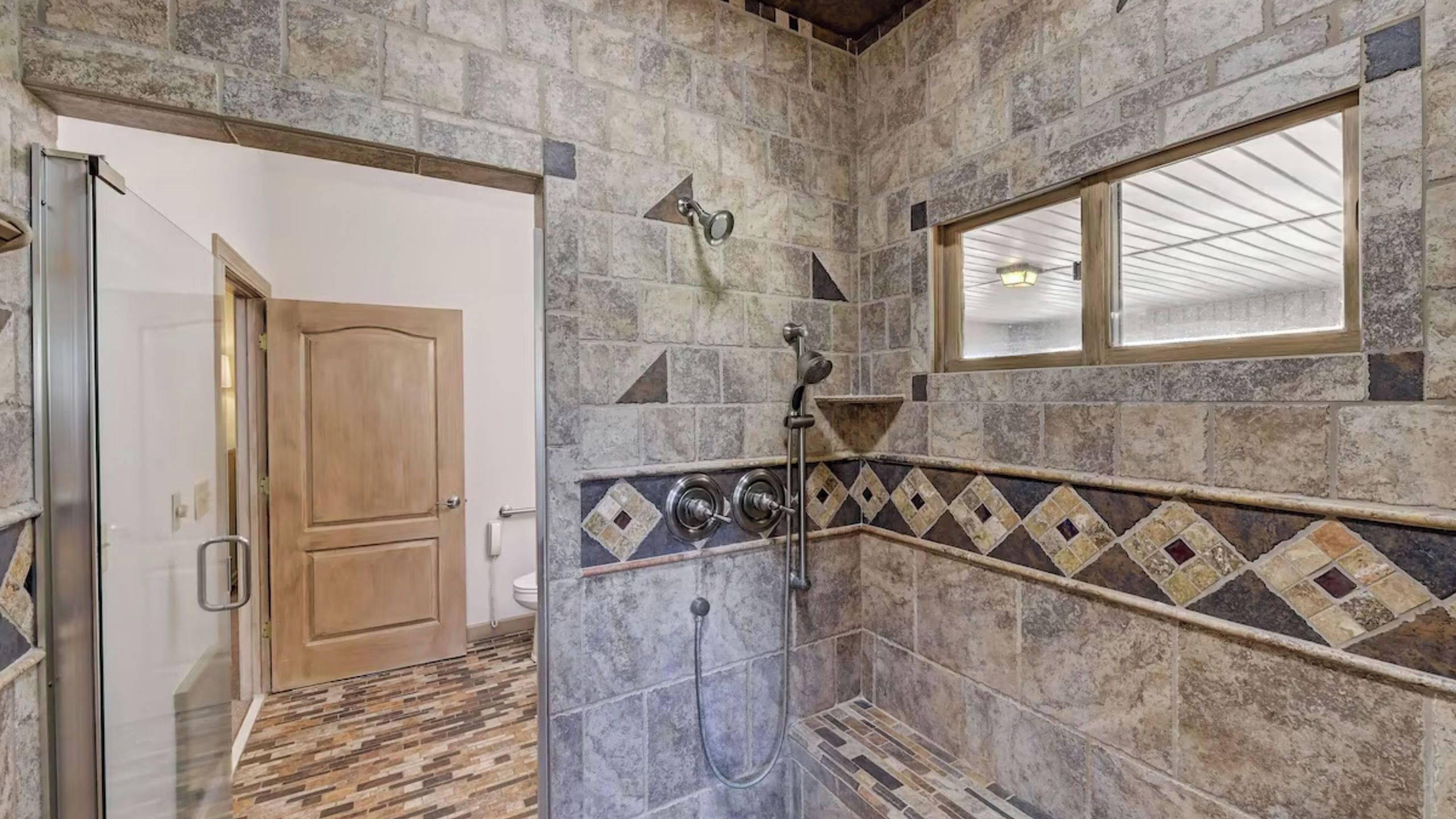 A bathroom with stone walls, a shower area, a wooden door, and a window.
