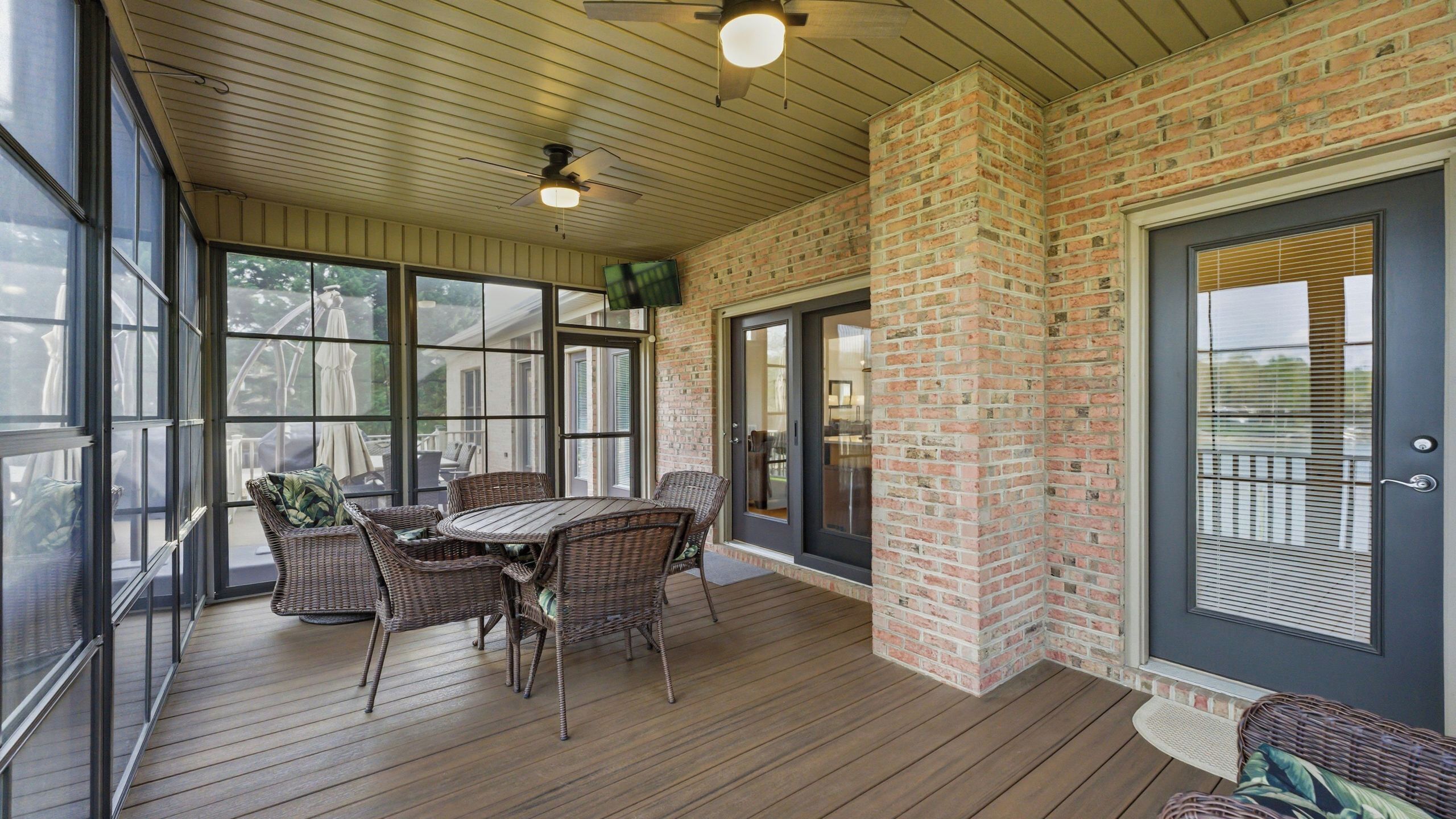 A covered patio with wicker furniture, a brick wall, and large windows.