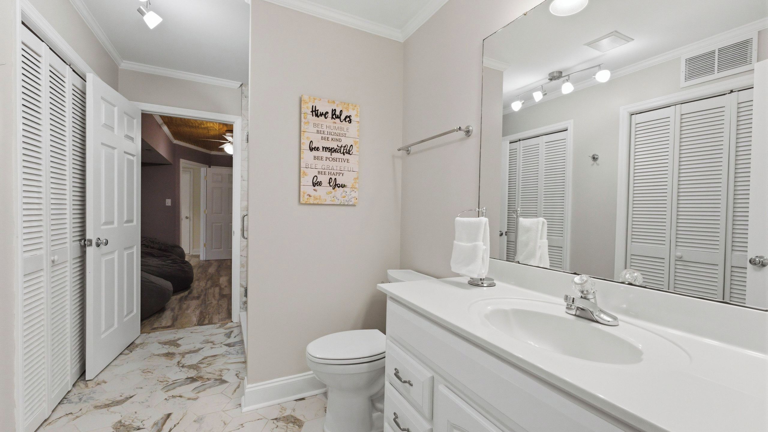 Une salle de bain avec un lavabo blanc, un miroir et des toilettes. Un panneau mural affiche des affirmations positives.