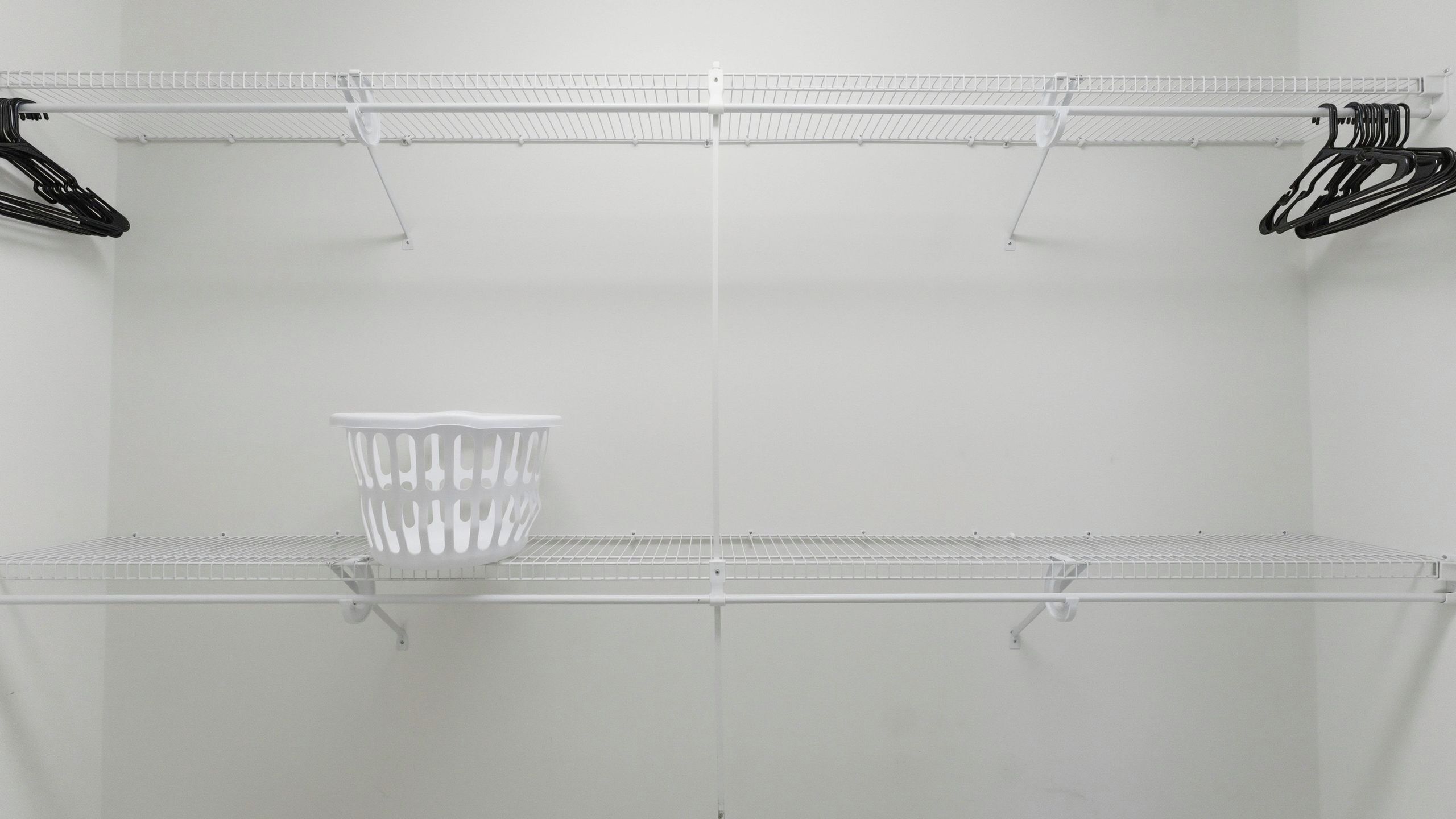 A white, empty storage closet with metal shelves and hooks.
