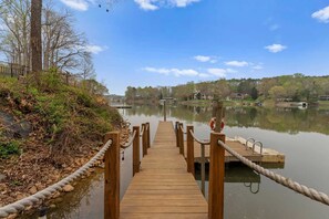A wooden pier leading to a calm lake with a dock and a lifebuoy on the right. - Sleeps 22, Lakefront w/ Private Dock & Pool, 2 Houses Lake Living by Avantstay (Sherrills Ford)