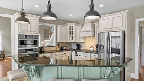 A spacious kitchen with white cabinetry, a central island with a glass top, stainless steel appliances, and pendant lighting.