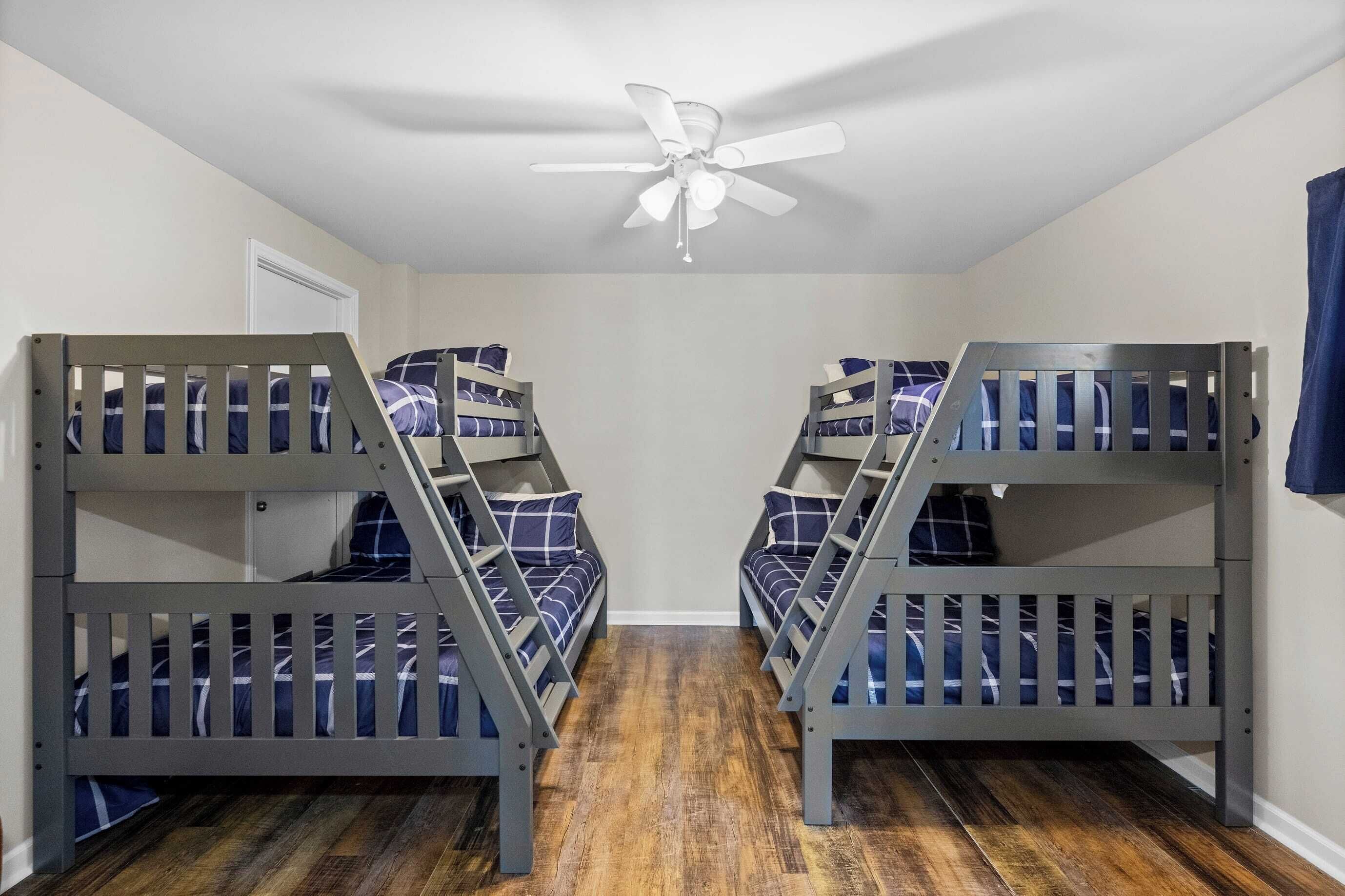 A room with four bunk beds, a ceiling fan, and a wooden floor.