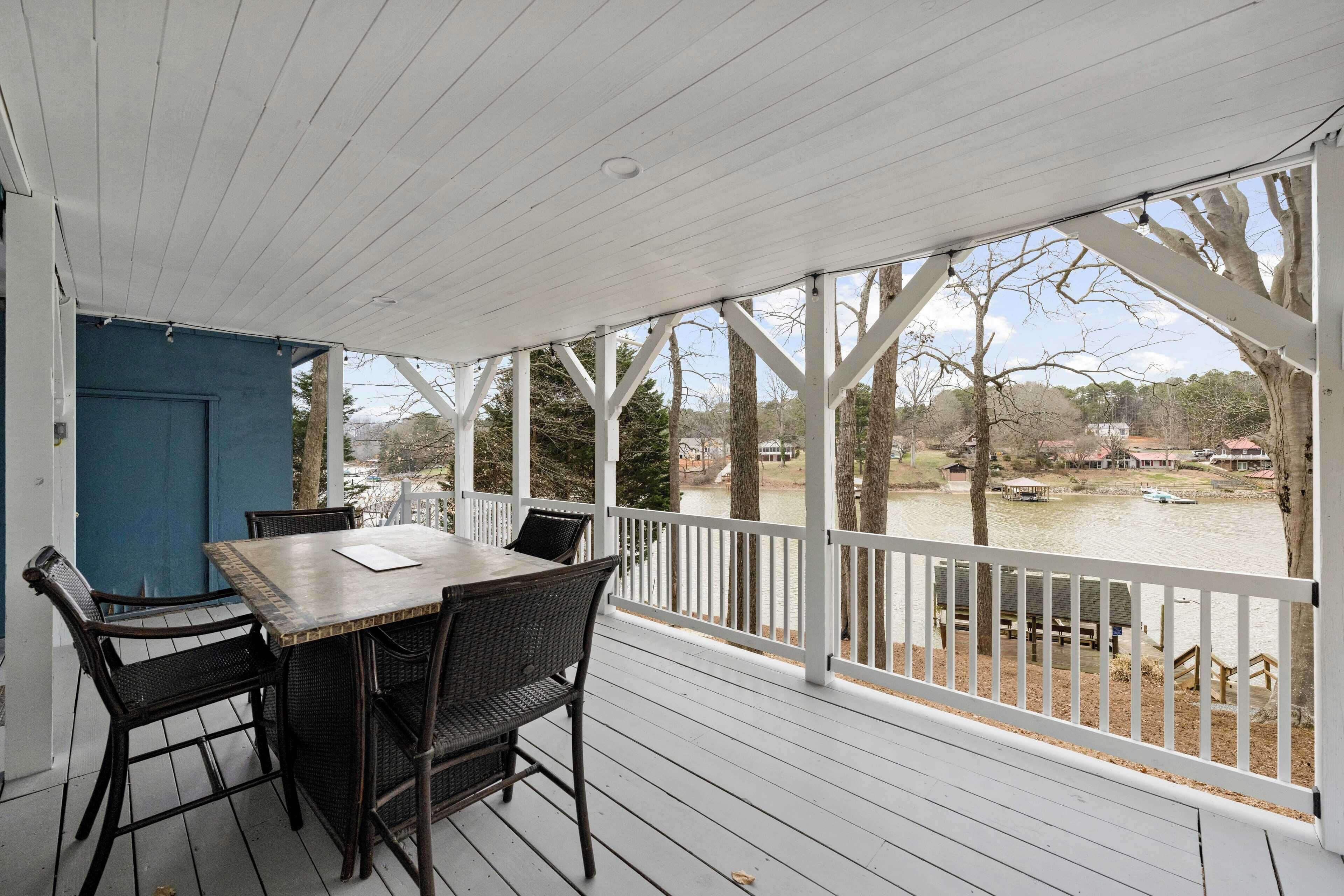 A covered outdoor area with a table and chairs, overlooking a body of water and trees.
