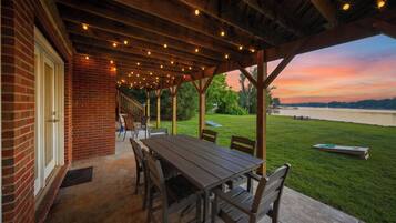 A covered patio with a table and chairs, overlooking a grassy area and a body of water.