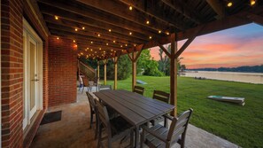 A covered patio with a table and chairs, overlooking a grassy area and a body of water.