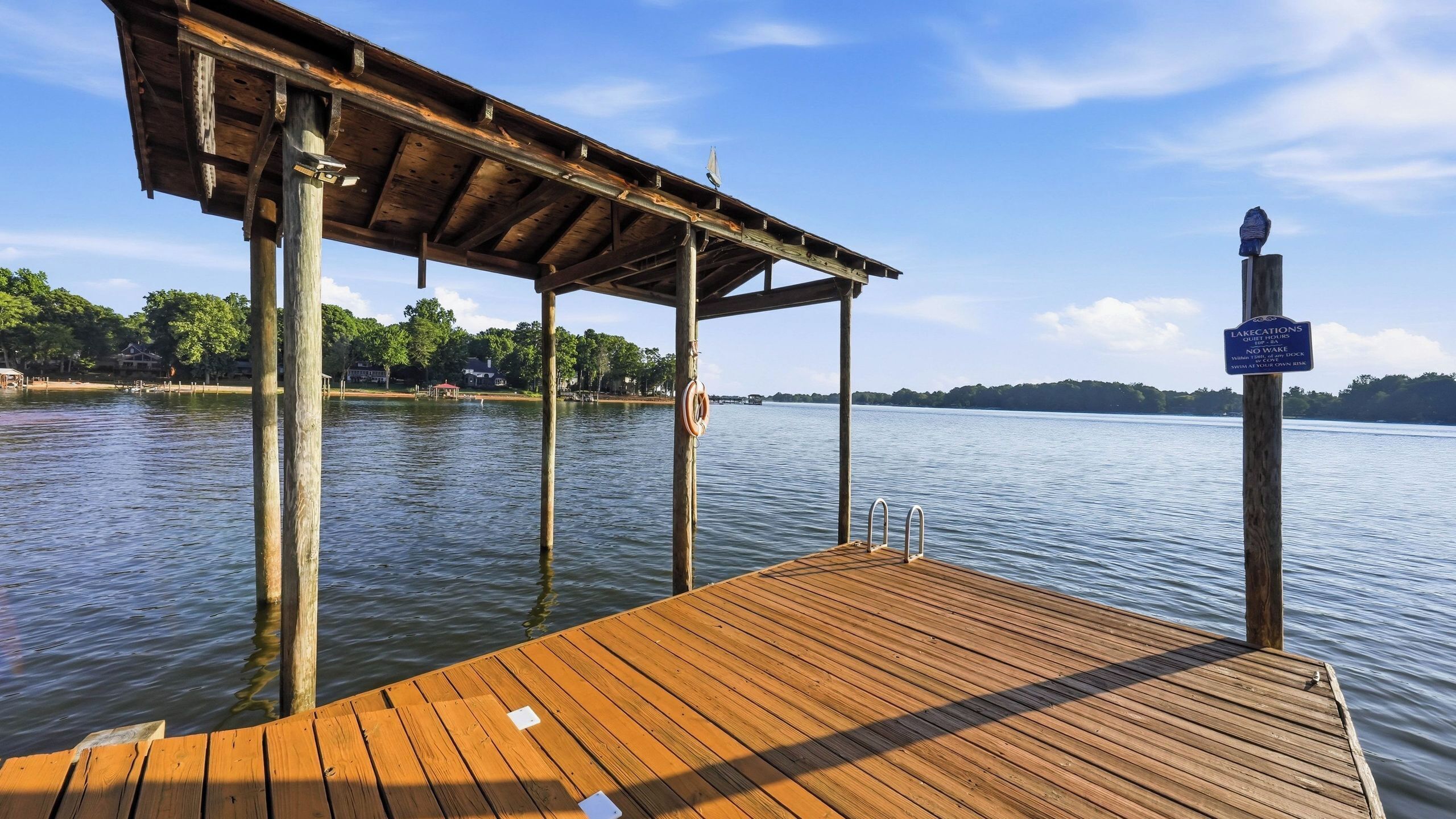 A wooden dock extending into calm water, with a covered area overhead and a signpost indicating lake regulations.
