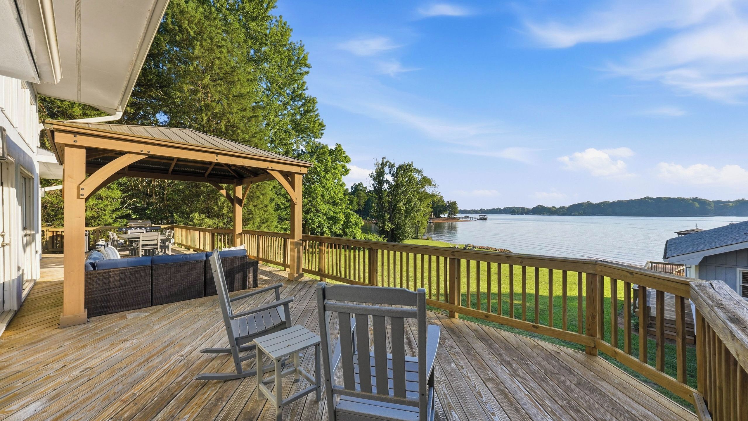 A wooden deck with outdoor furniture, a pergola, and a view of a lake.