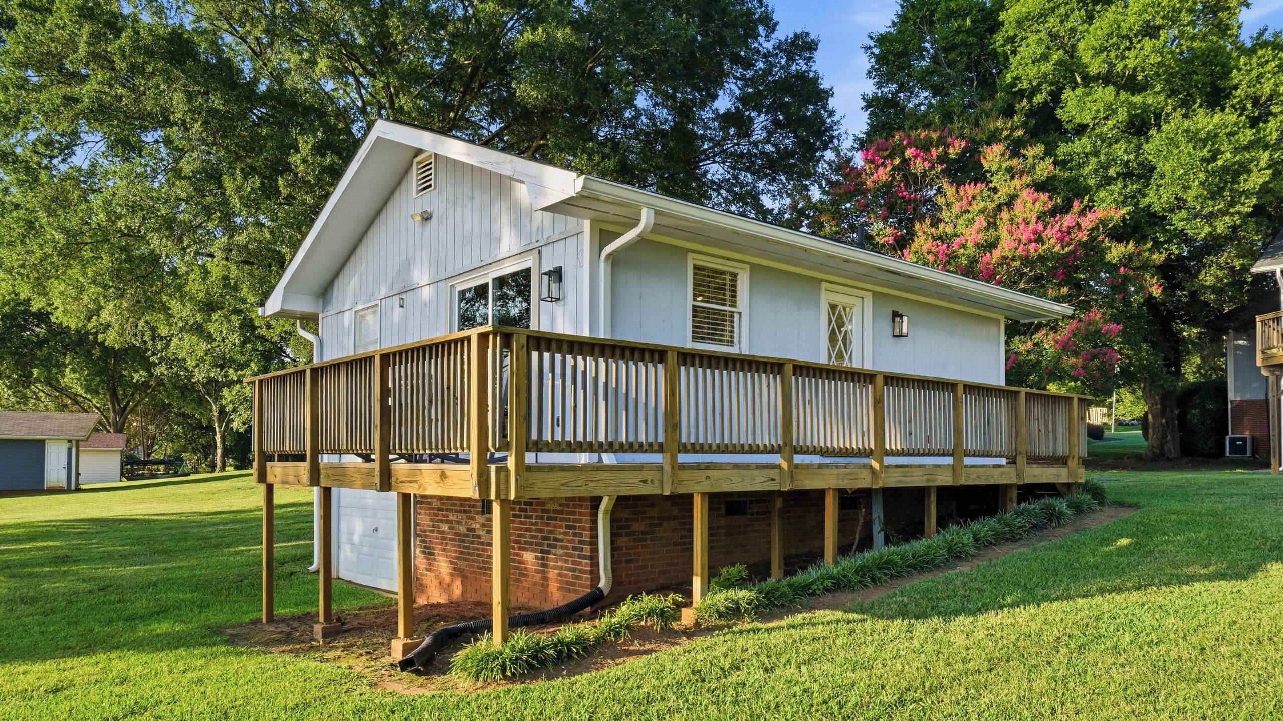 A two-story house with a deck, surrounded by trees and grass.