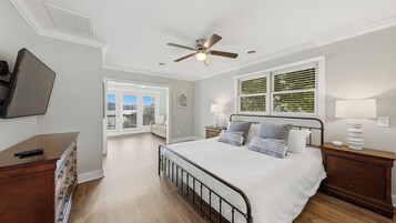 Un dormitorio con cama, cómoda, mesitas de noche, ventilador de techo y ventana con persianas.