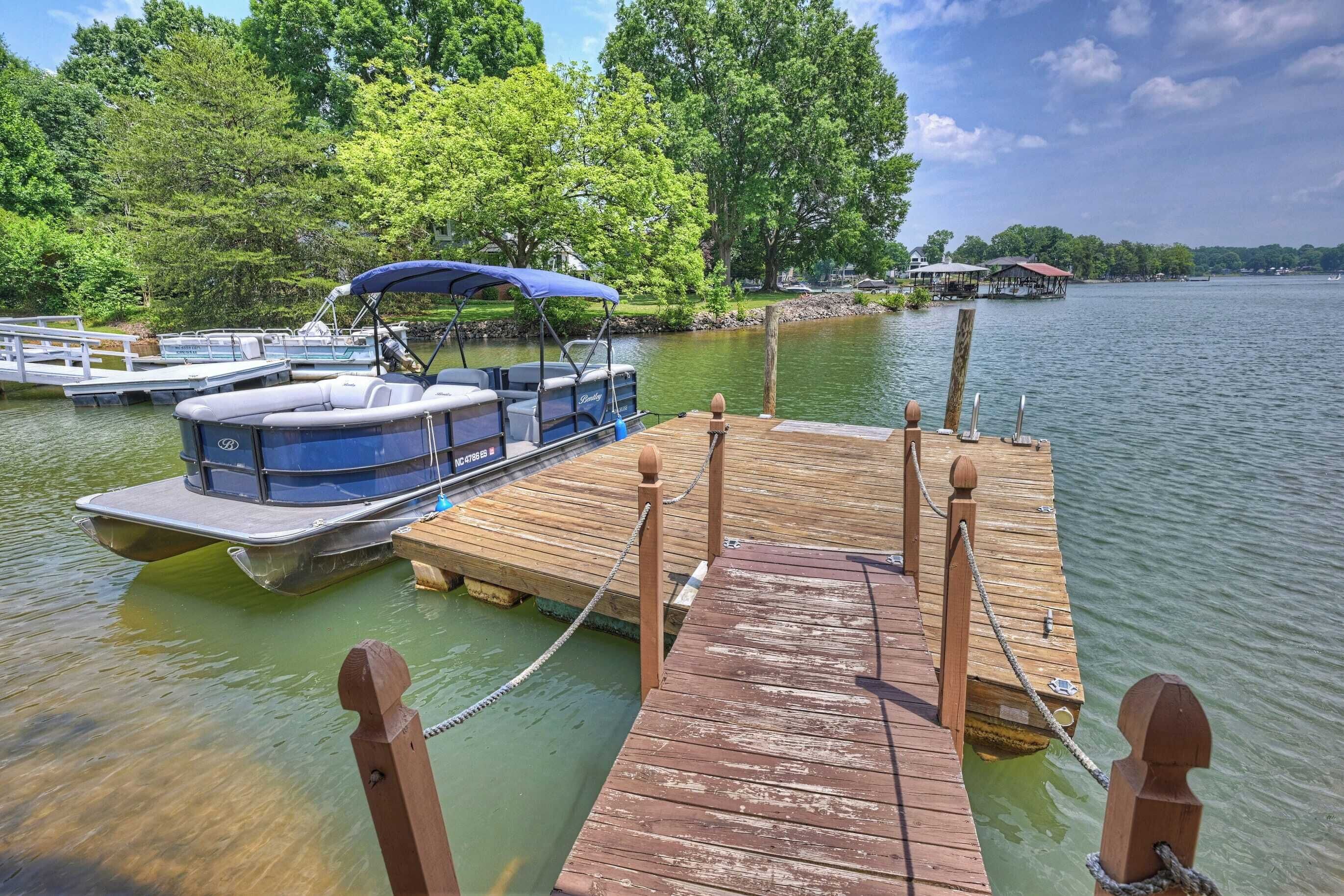 A wooden dock with a boat docked at the pier, surrounded by trees and a calm lake.