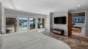 Ein Schlafzimmer mit einem großen Bett, einem an der Wand montierten Fernseher und Blick auf einen Swimmingpool durch Glastüren.
