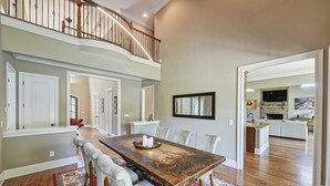 A spacious dining area with a long table, cushioned chairs, and a wooden floor. A staircase leads to an upper level. - Dock Holiday by Avantstay Custom Home + New Dock (Huntersville)