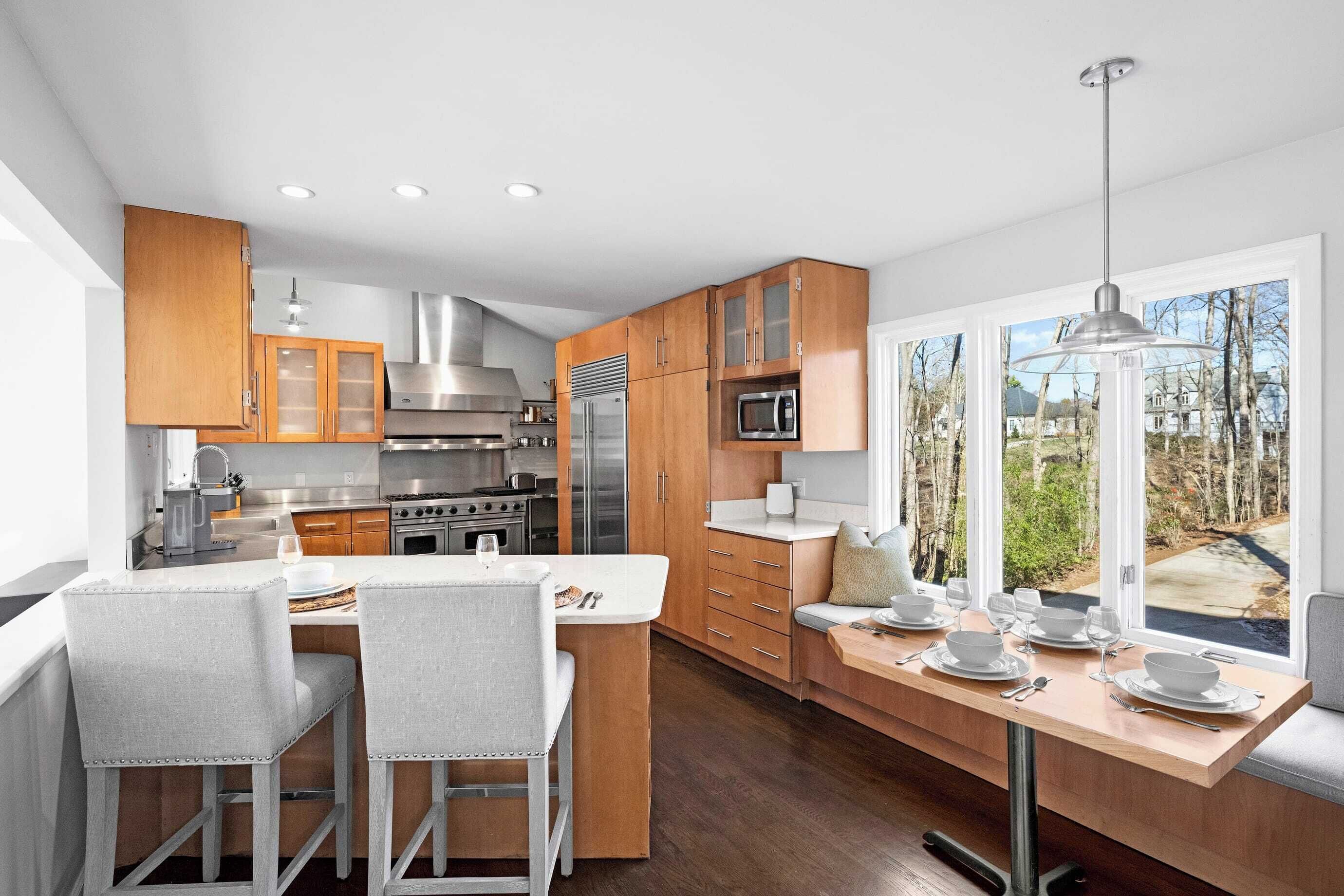 A modern kitchen with wooden cabinets, stainless steel appliances, and a dining area with a view of the outdoors.