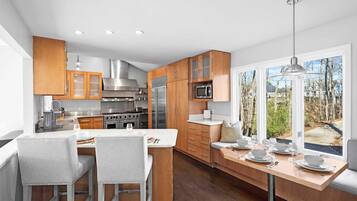 A modern kitchen with wooden cabinets, stainless steel appliances, and a dining area with a view of the outdoors.