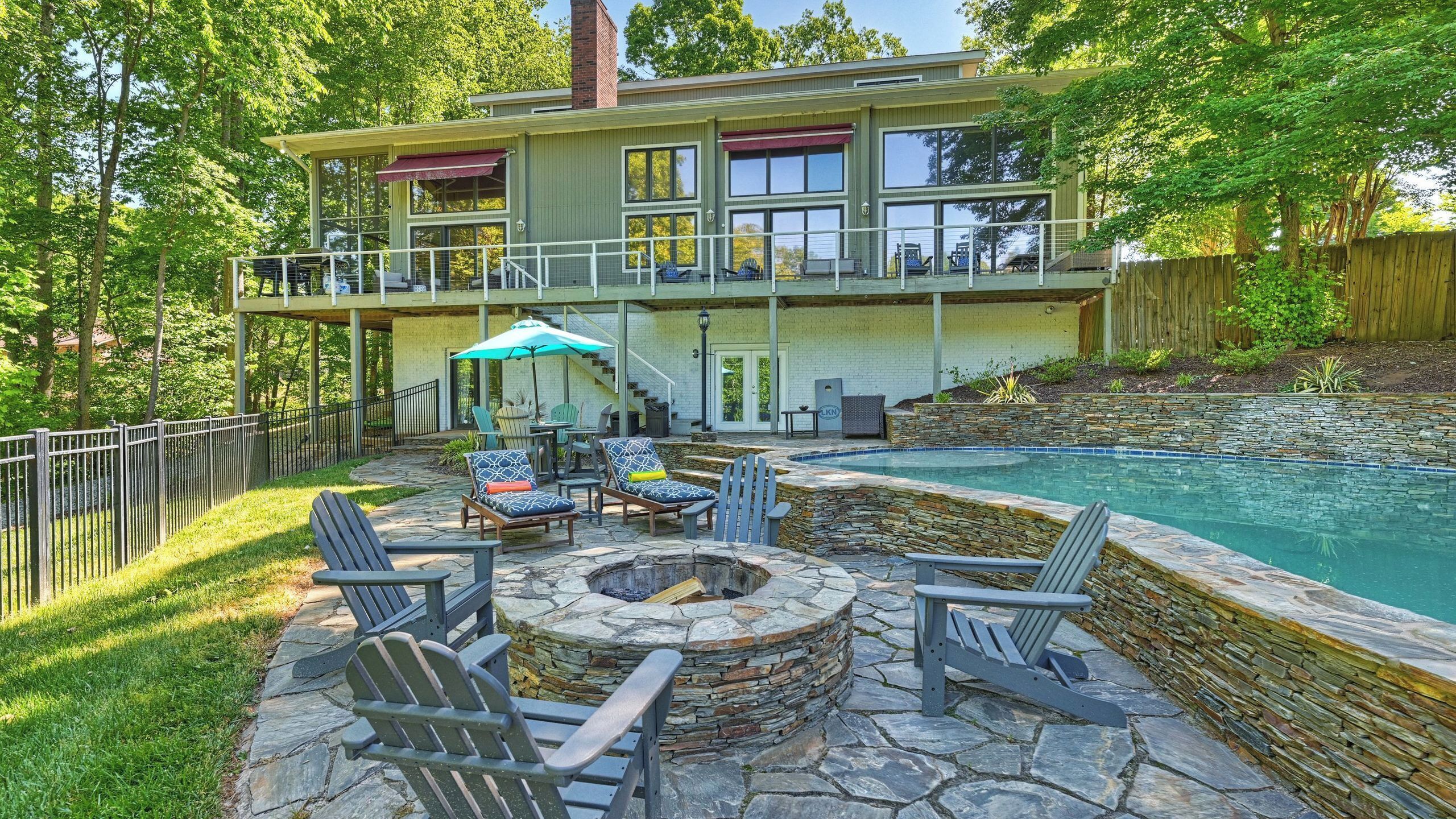 A two-story house with a pool, outdoor seating, and a fire pit.