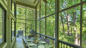 Un espace repas abrité, avec une table dressée pour quatre personnes, donnant sur une zone boisée.