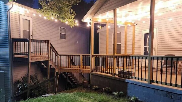 Une maison à deux étages dotée d’une terrasse en bois et d’un porche couvert, entourée d’une cour verdoyante.