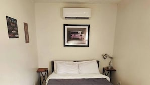 Une chambre à coucher avec un lit, un plancher en bois, un climatiseur fixé au mur et deux tables de chevet avec des lampes.