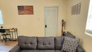 Un canapé modulable avec un repose-pieds, placé dans un salon doté d’un plancher en bois, d’une porte et d’un drapeau américain accroché au mur.
