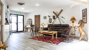 Un salón acogedor con un sofá de cuero oscuro, una mesa de centro de madera y una alfombra roja con estampado. Hay esquíes apoyados en la pared y un caballo balancín de madera.