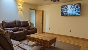 Una sala de estar con un sofá de cuero marrón, una mesa de centro de madera y un televisor grande montado en la pared.