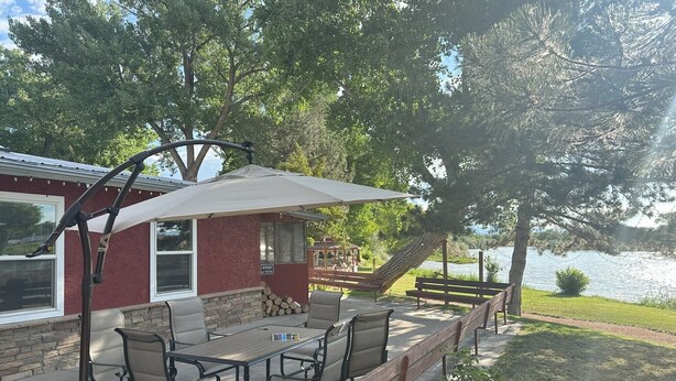 Un patio al aire libre con una mesa y sillas, una zona de estar cubierta y vistas a un lago.