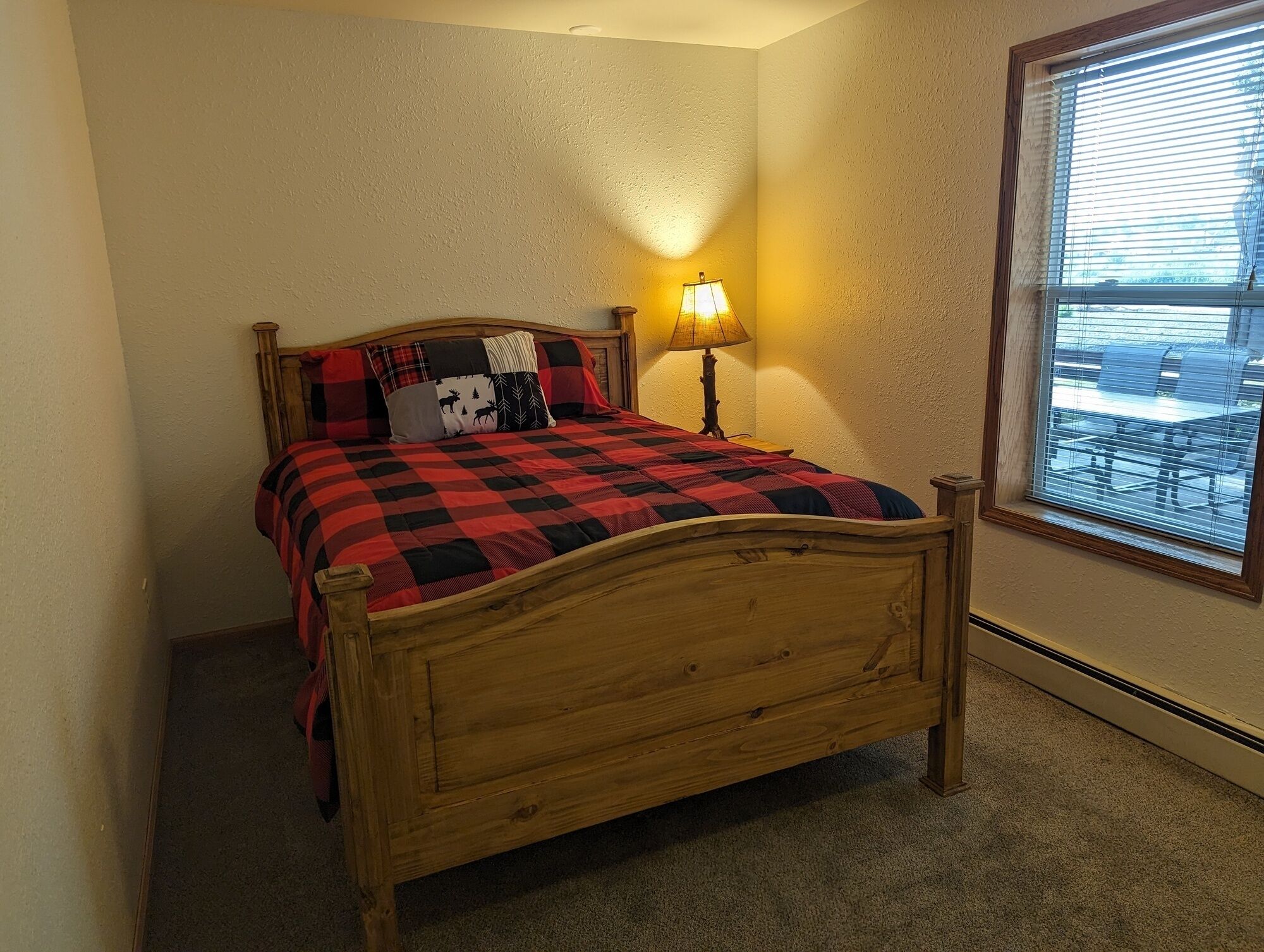 A bedroom with a wooden bed, a red and black checkered bedspread, and a nightstand with a lamp.