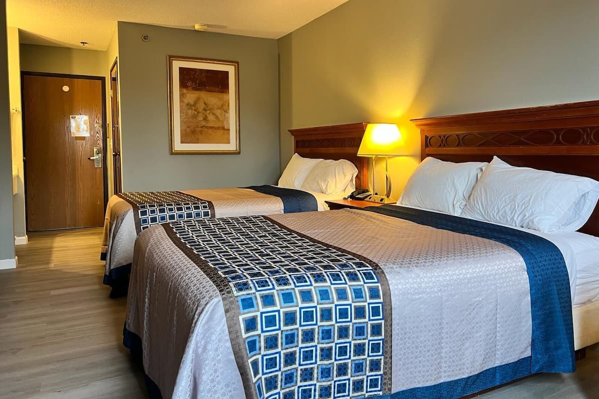 A hotel room with two beds, a wooden headboard, a framed picture on the wall, and a bedside lamp.