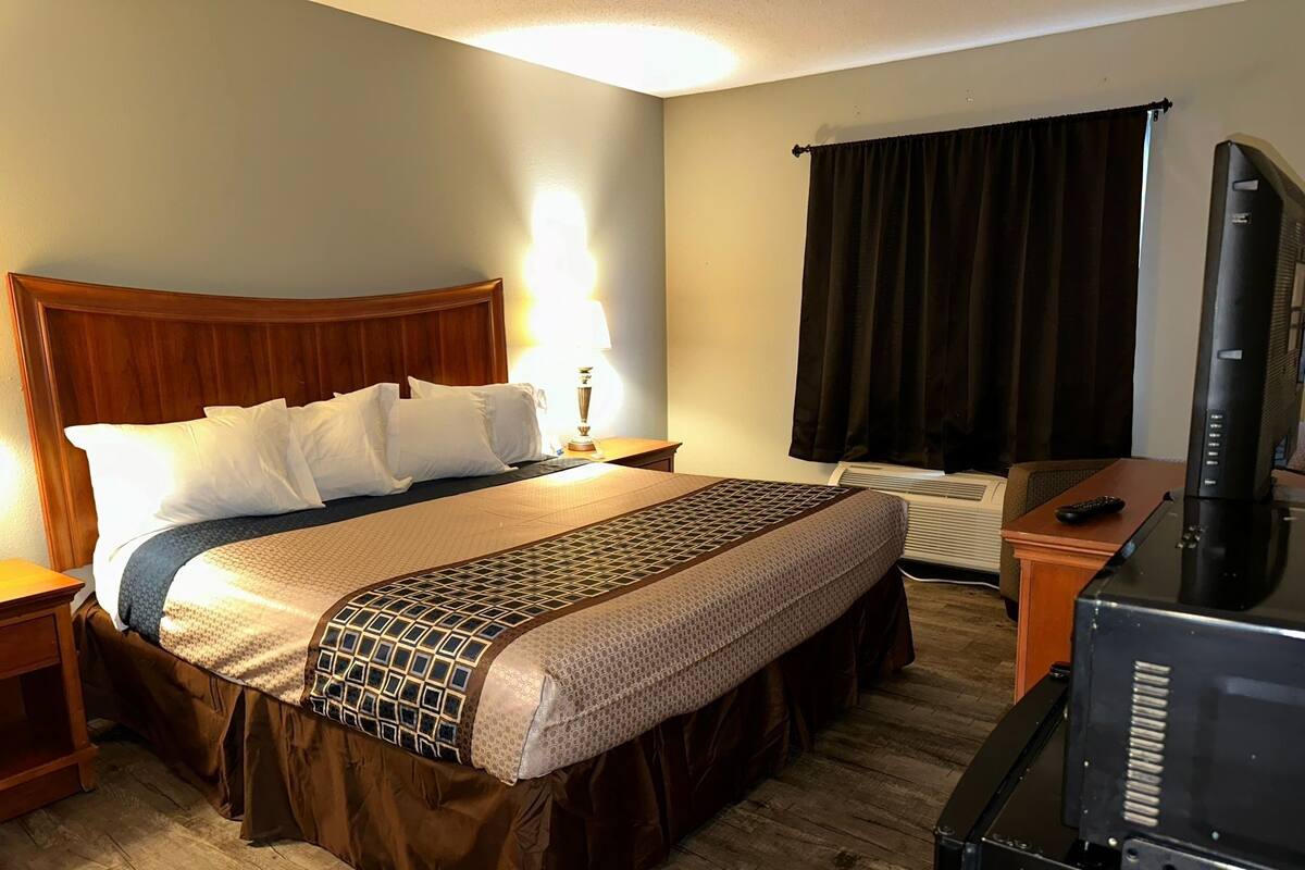 A hotel room with a bed, a TV, a heater, and a lamp.