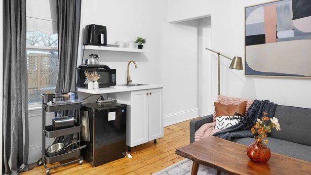 Un espace de vie compact comprenant un coin cuisine, un canapé, une table basse et un grand tableau abstrait.