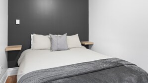 Une chambre à coucher avec un lit, deux tables de chevet, une couverture grise et un mur de couleur sombre.